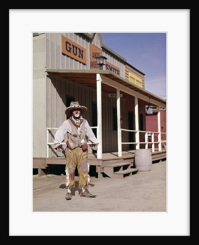 1960s sad clown in cowboy costume standing in street of western frontier town by Anonymous