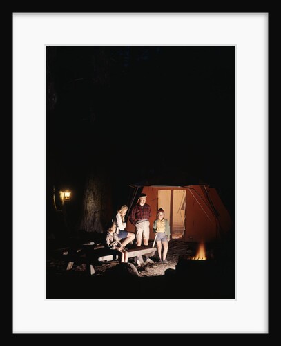 1960s night scene family gazing into campfire by tent by Anonymous