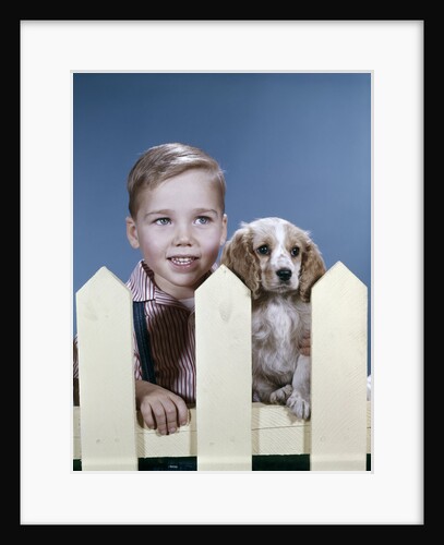 1960s boy puppy dog looking over white picket fence by Anonymous