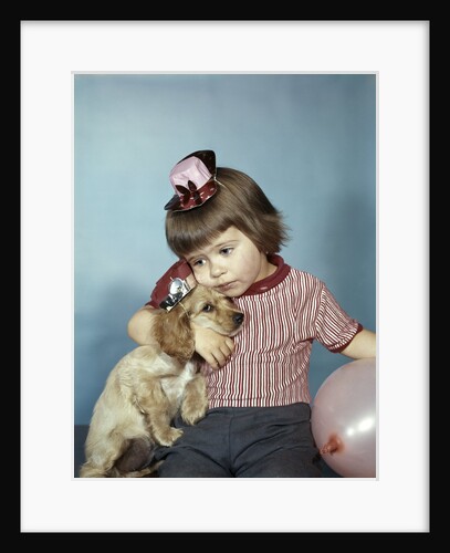 1950s 1960s little girl wearing party hat frowning hugging a cocker spaniel puppy by Anonymous