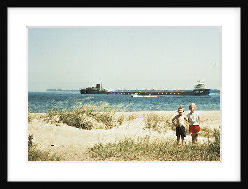 1950s young boy and girl on beach smiling with a tanker ship on lake behind them port huron michigan 1955 by Anonymous