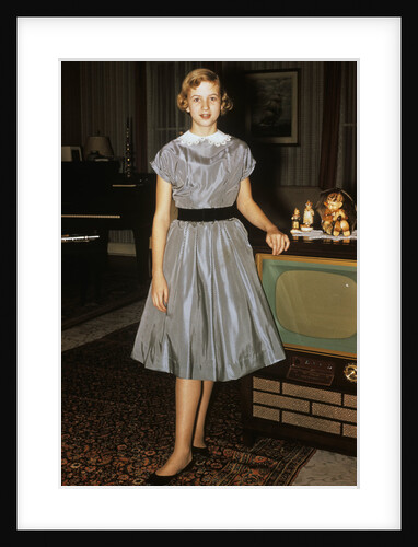 1950s teenage girl dressed for her first date in gray silky dress posed by television set by Anonymous