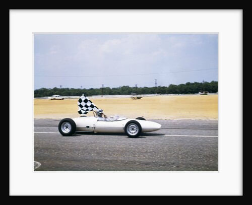 1960s race car driver in lotus ford car taking victory lap holding checkered flag by Anonymous