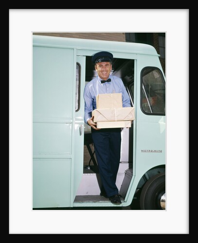 1950s 1960s man driver delivery truck van step out vehicle door holding packages boxes uniform hat service deliver work by Anonymous