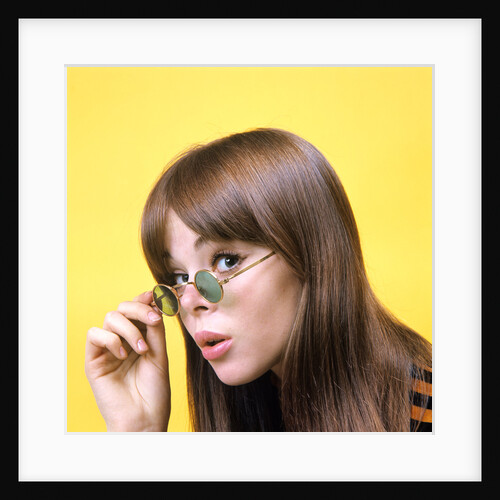 1960s portrait young brunette woman wear granny sunglasses surprised doubtful facial expression yellow background by Anonymous