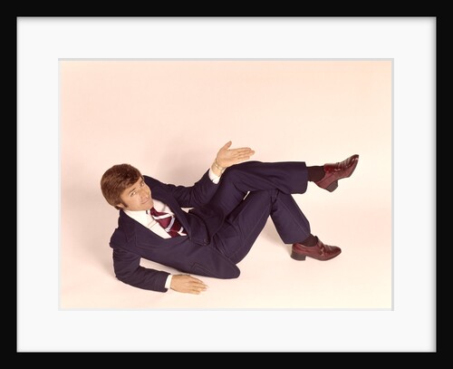 1970s overhead looking down at man lying down legs crossed wearing business suit shrug off hand expression looking at camera by Anonymous