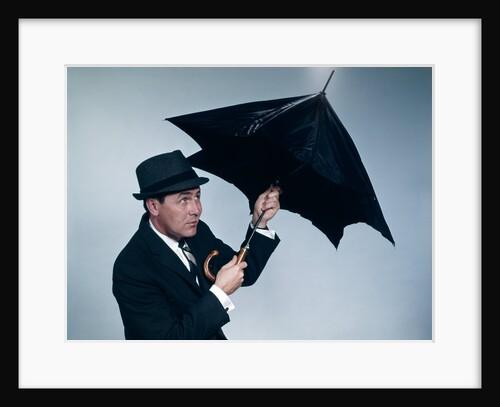 1960s businessman wearing hat opening umbrella to protect from rain by Anonymous