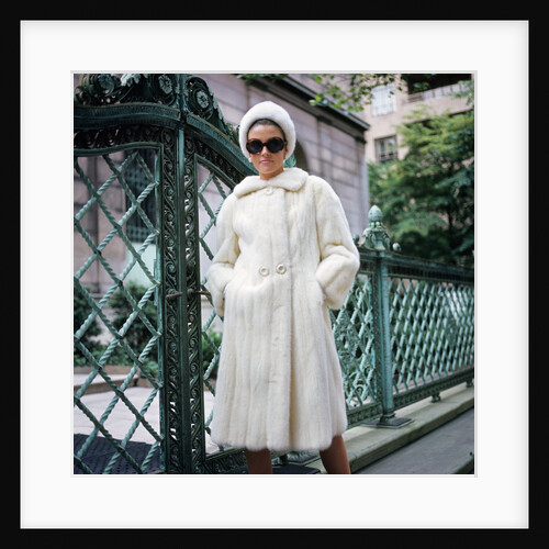 1960s woman wearing white mink fur coat hat sunglasses by wrought iron gate by Anonymous