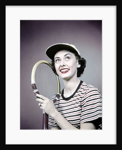 1950s smiling brunette woman holding tennis racket wearing striped t-shirt and sports cap by Anonymous