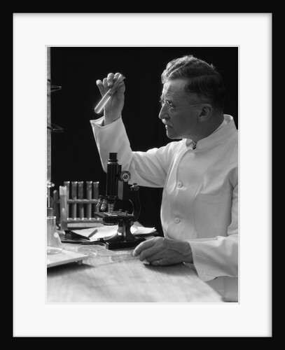 1920s 1930s 1940s scientist lab technician in white coat looking at test-tube in front of microscope by Anonymous