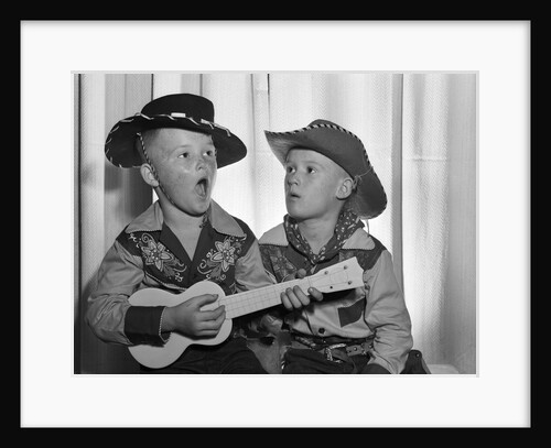 1950s 2 juvenile boys in cowboy hat & shirts playing ukulele & singing mouth open wide by Anonymous