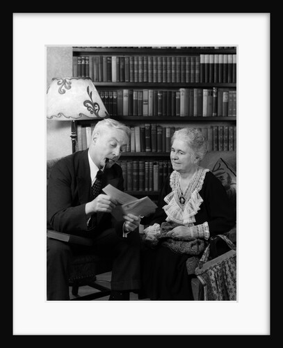 1930s 1940s retired senior couple looking at check in living room man smoking pipe by Anonymous