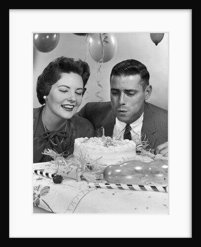 1950s 1960s couple with birthday anniversary cake man blowing out candle by Anonymous