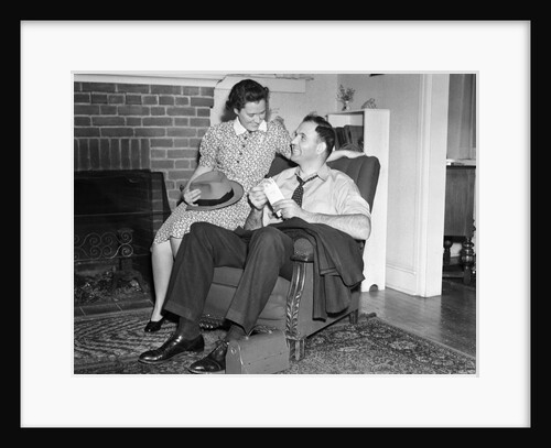 1940s smiling man sitting in chair holding pay envelope while wife sits on arm of chair holding his hat lunch box oriental rug by Anonymous