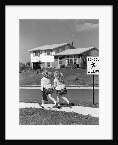 1950s back view of twin girls in plaid skirts & cardigans holding book bags running past school slow sign by Anonymous