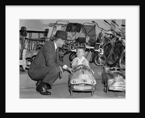 1950s father in toy store purchasing for son driving toy convertible peddle car by Anonymous