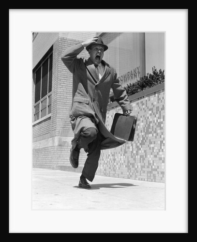1960s 1950s frantic man running down street holding hat on with hand carrying briefcase wearing top coat by Anonymous