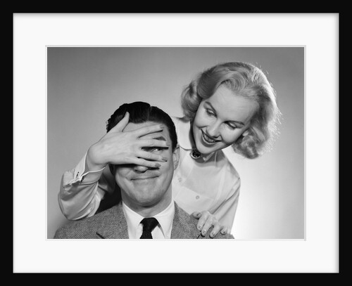 1950s woman standing behind man with hand over his eyes by Anonymous