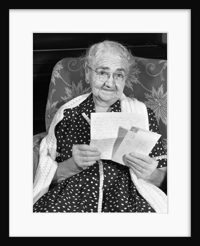1960s elderly woman in polka-dotted dress & shawl reading letter by Anonymous