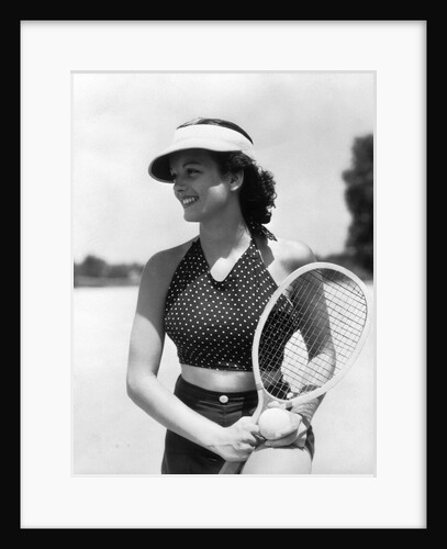 1930s woman in polka dot halter top shorts & sun visor holding a tennis ball & racket by Anonymous