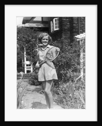 1930s teen girl brunette on sidewalk of house holding tennis racket wearing shorts by Anonymous
