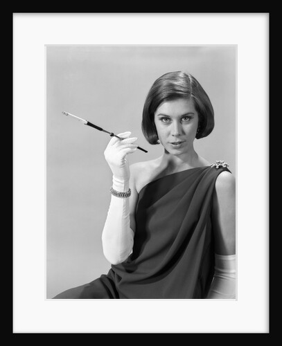1960s formally elegantly dressed young woman looking at camera with a cigarette holder wearing long white gloves by Anonymous