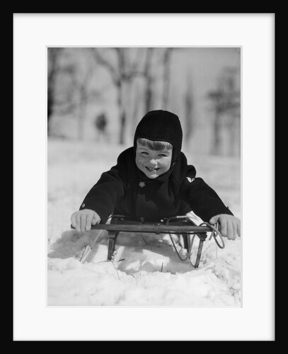 1930s young smiling boy on sled in snow looking at camera by Anonymous