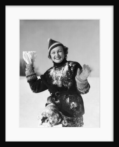 1930s smiling young woman covered in snow throwing piece of snow squinting looking at camera by Anonymous