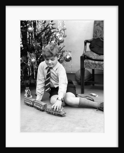 1930s young boy playing with toy train by christmas tree by Anonymous