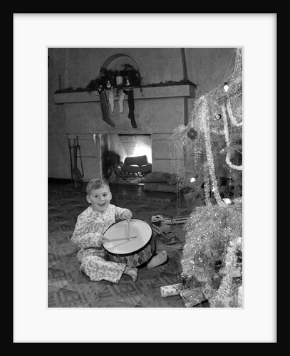1950s little boy playing toy drum by christmas tree and fireplace looking at camera by Anonymous