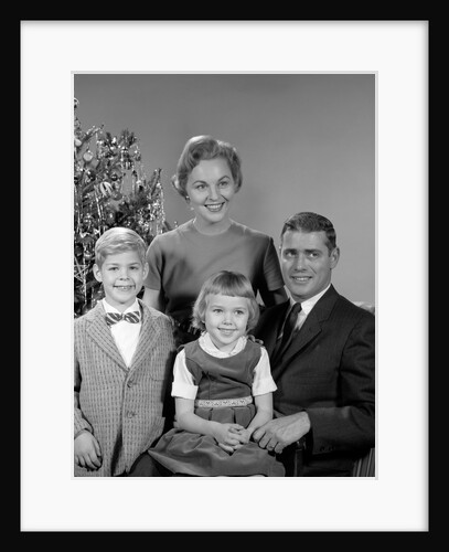 1950s 1960s family portrait smiling father mother daughter son sitting together in front of indoor christmas tree by Anonymous