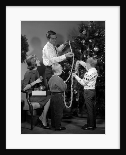 1960s family father mother two sons trimming christmas tree with string of popcorn by Anonymous