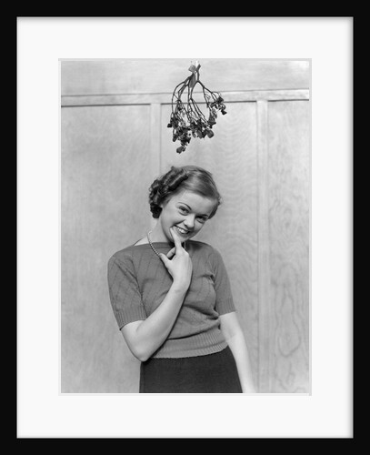 1930s 1940s cute young woman standing under mistletoe smiling hand near mouth looking at camera by Anonymous