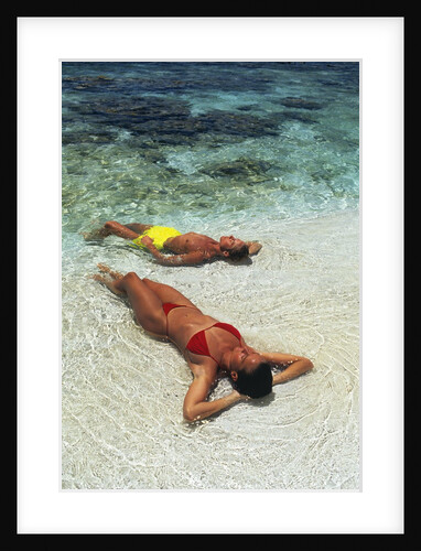 1990s Couple Sunbathing In Shallow Water At The Ocean's Edge by Anonymous