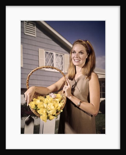 1960s Smiling Woman Holding Basket Yellow Flowers House Background by Anonymous