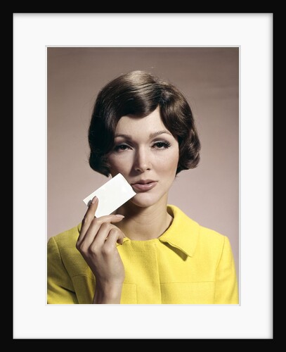 1960s Brunette Woman Holding Blank Business Card To Face Looking At Camera Wearing Yellow Top by Anonymous
