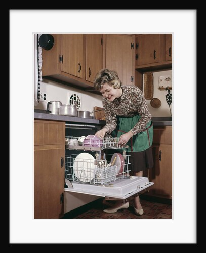 1960s Smiling Woman Apron Bending Over Emptying Dishwasher In Kitchen by Anonymous