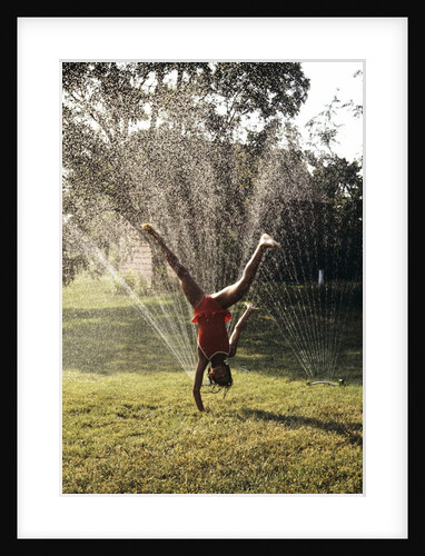 1980s Little Girl Cart Wheeling Through Lawn Sprinklers by Anonymous