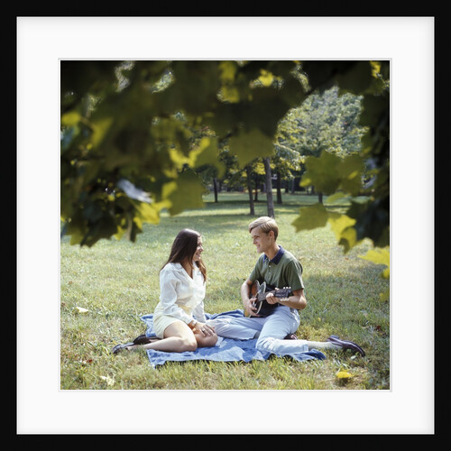 1960 1960s 1970 1970s Retro Smiling Couple Man Woman Sitting On Blanket On Grass Park Man Playing Acoustic Guitar by Anonymous