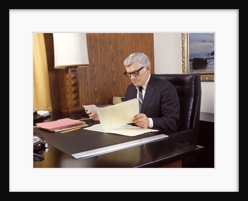 1960 1960s 1970 1970s Mature Man Silver Gray Grey Hair Executive Seated Desk Reading Business Papers Men Executives by Anonymous