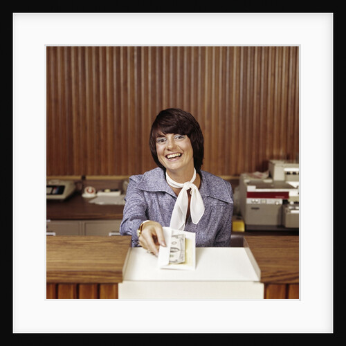 1970s Smiling Woman Bank Teller Handing Cash Over Counter by Anonymous