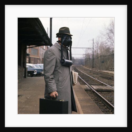 1950s Man Wearing Gas Mask Hat At Commuter Train Station Holding Briefcase Newspaper by Anonymous
