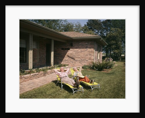 1960s Senior Couple Lawn Chairs Relaxing In Yard Of A Brick House by Anonymous