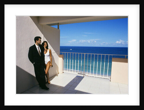 1990s Man In Dark Suit And Tie And Woman In White One Piece Bathing Suit Standing Together On Ocean Side Sun Deck by Anonymous