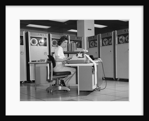 1960s Woman In Mainframe Computer Room Surrounded By Many Data Tape Drives Sitting At Desk Typing On Typewriter Indoor by Anonymous