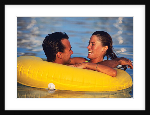 1980s Happy Young Couple Floating Together In Yellow Plastic Inner Tube In A Pool by Anonymous