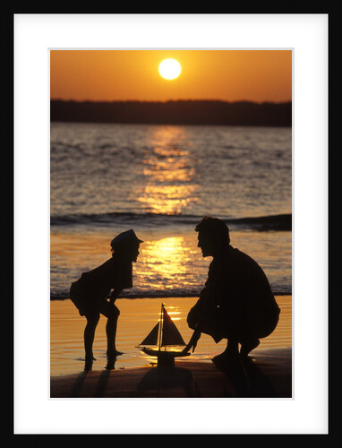 1990s Anonymous Father And Son Playing With Toy Boat At The Beach Silhouetted Against Setting Sun by Anonymous