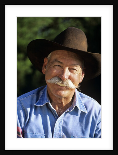 1990s Portrait Of Smiling Cowboy With Gray Mustache Black Hat Blue Shirt Looking At Camera by Anonymous