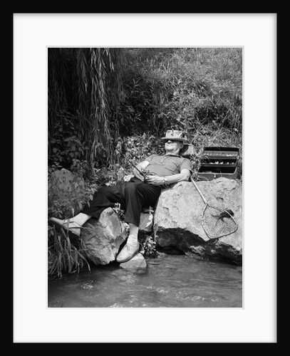 1950s Lazy Fisherman Lying Back On Rock With Hat Pulled Over Eyes Fishing In Creek by Anonymous