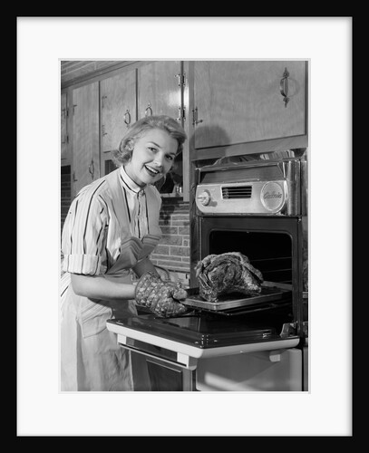 1950s Smiling Woman Housewife Wearing Apron Taking Large Roast Beef From Electric Oven In Kitchen Looking At Camera by Anonymous